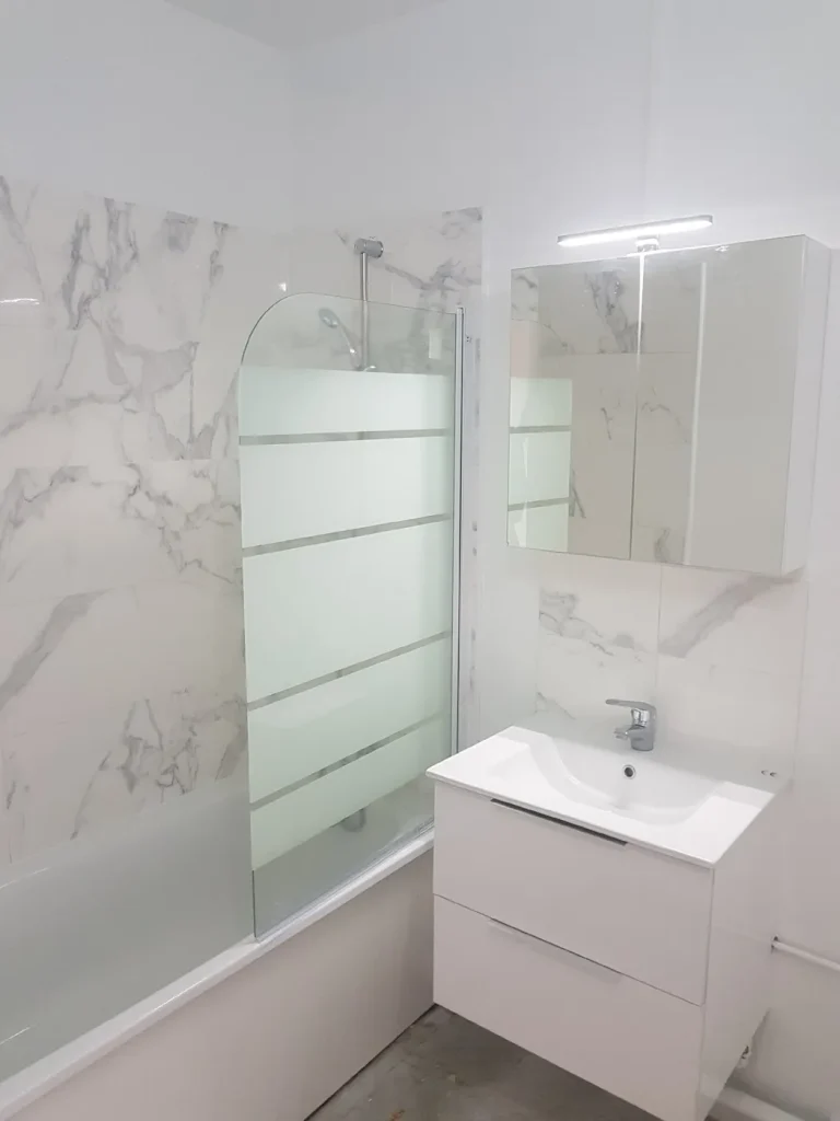 Salle de bains rénovée avec baignoire, pare-bain et meuble vasque blanc